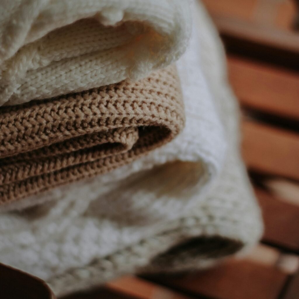 Close-up of neatly stacked beige and white wool blankets on a wooden chair.