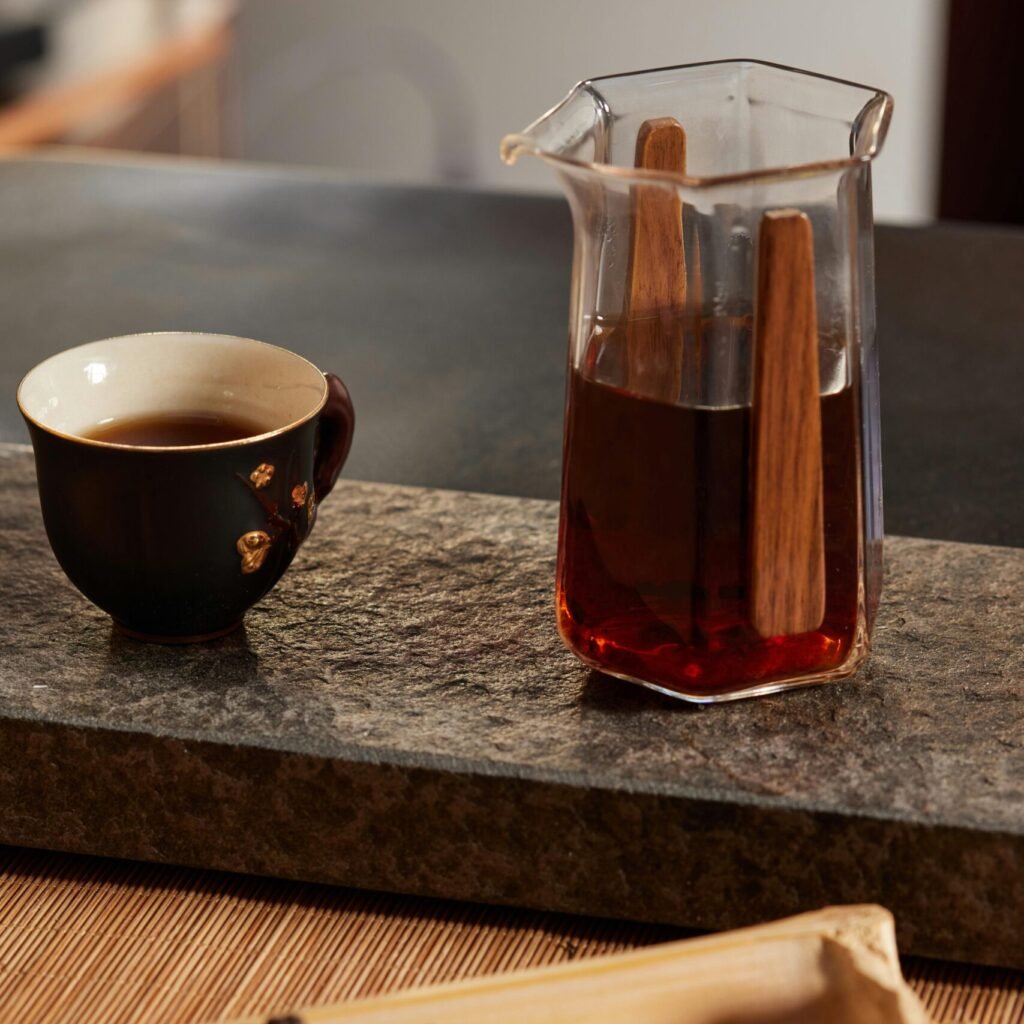 A beautiful tea setup featuring a glass server, a black tea cup, and tea leaves on a bamboo tray.